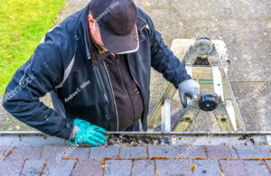 A man on a ladder cleaning out gutters